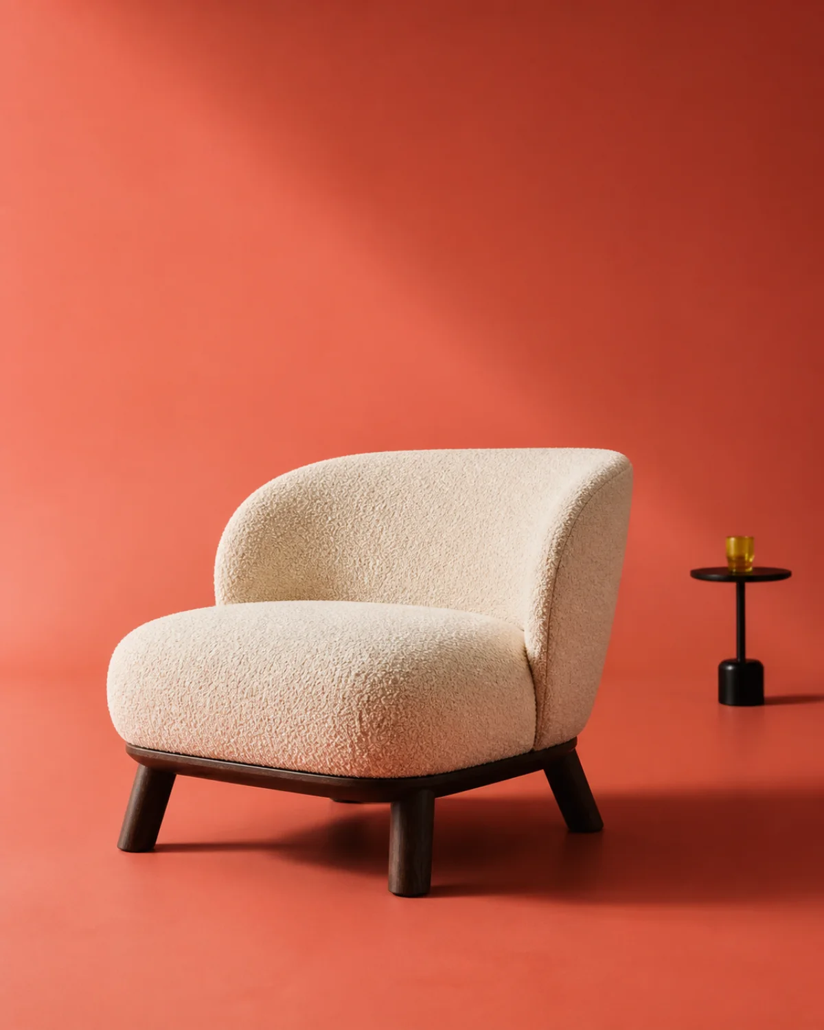 A sculptural cream boucle lounge chair on a coral studio backdrop